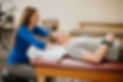 Physical Therapist smiles while using manual therapy techniques on the shoulders of a patient.